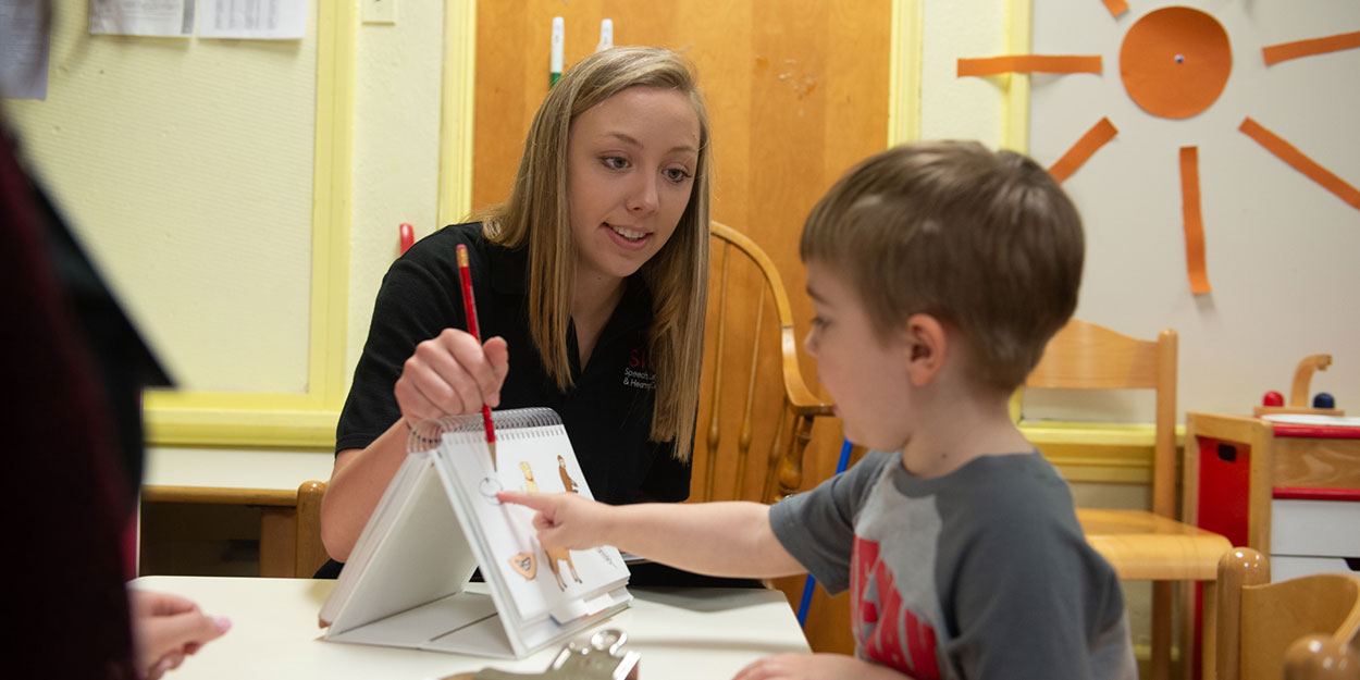 A teacher working with a young child on recognizing an image on a notepad